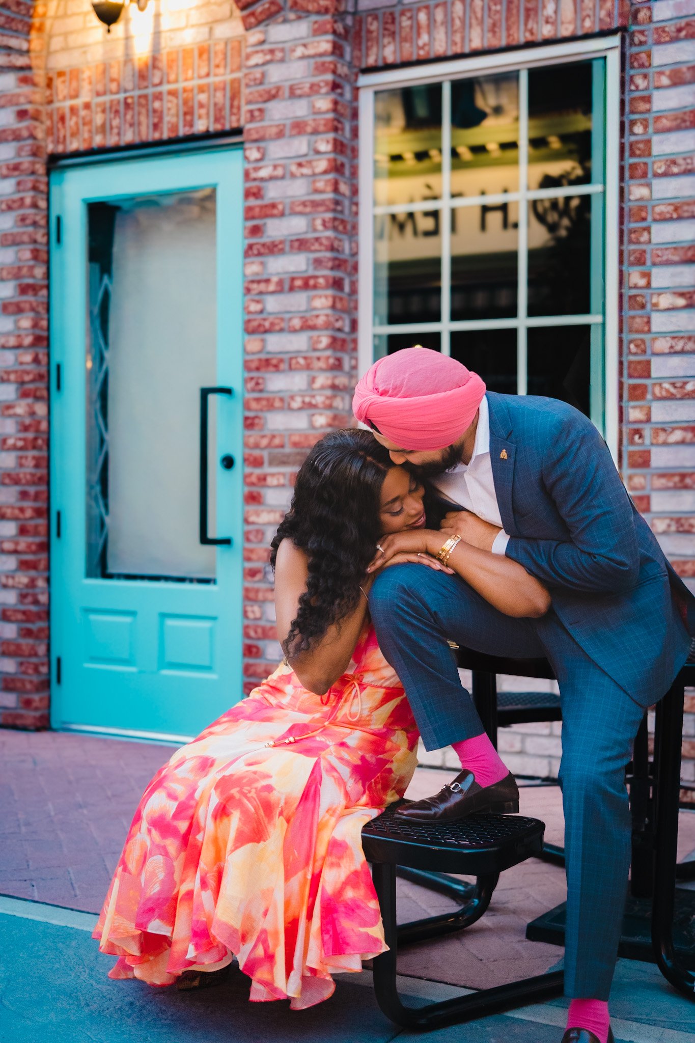 Couple kissing at a teal doorway, groom in a pink turban and bride in pink