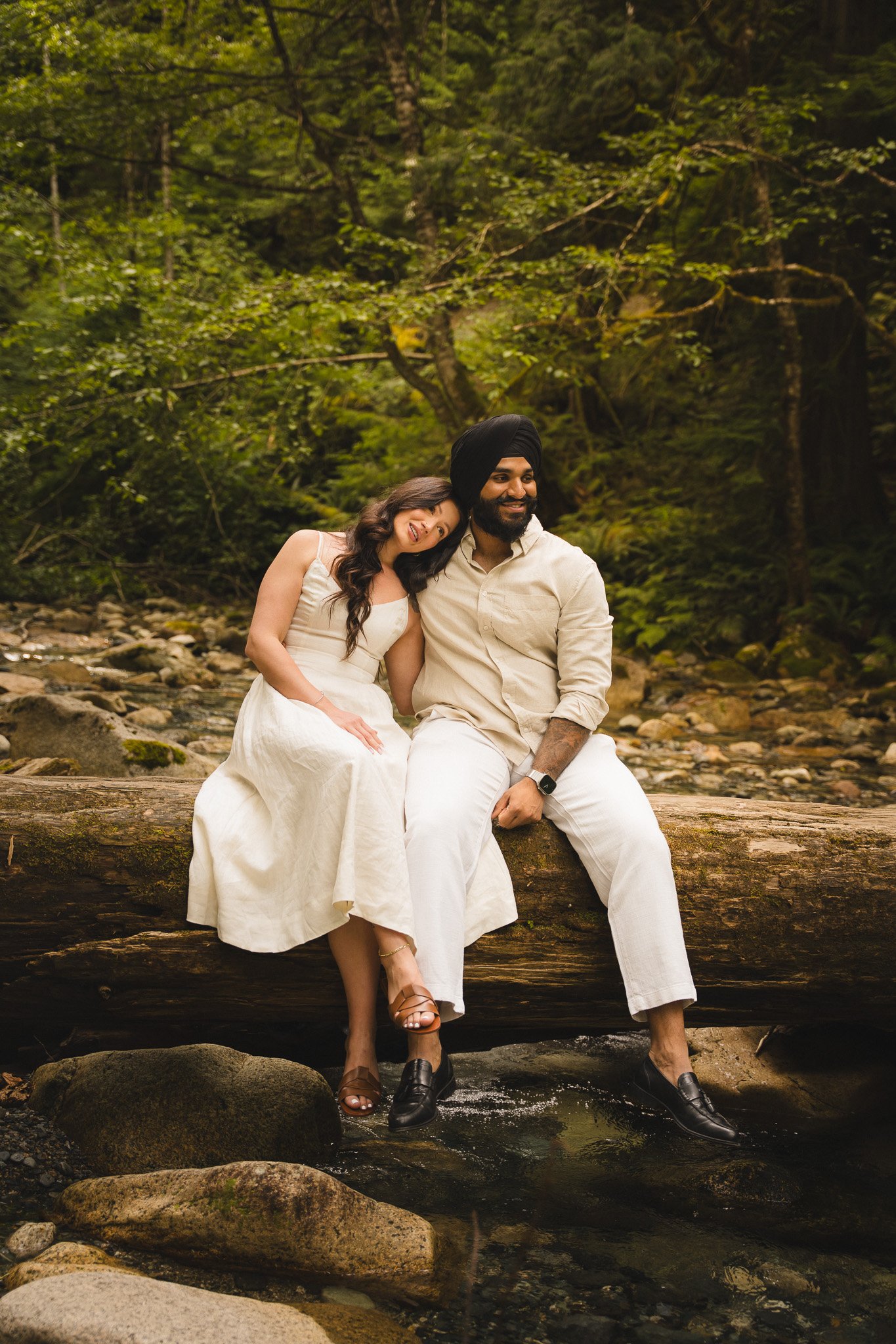 Couple in cream outfits sitting on rocks by a forest stream