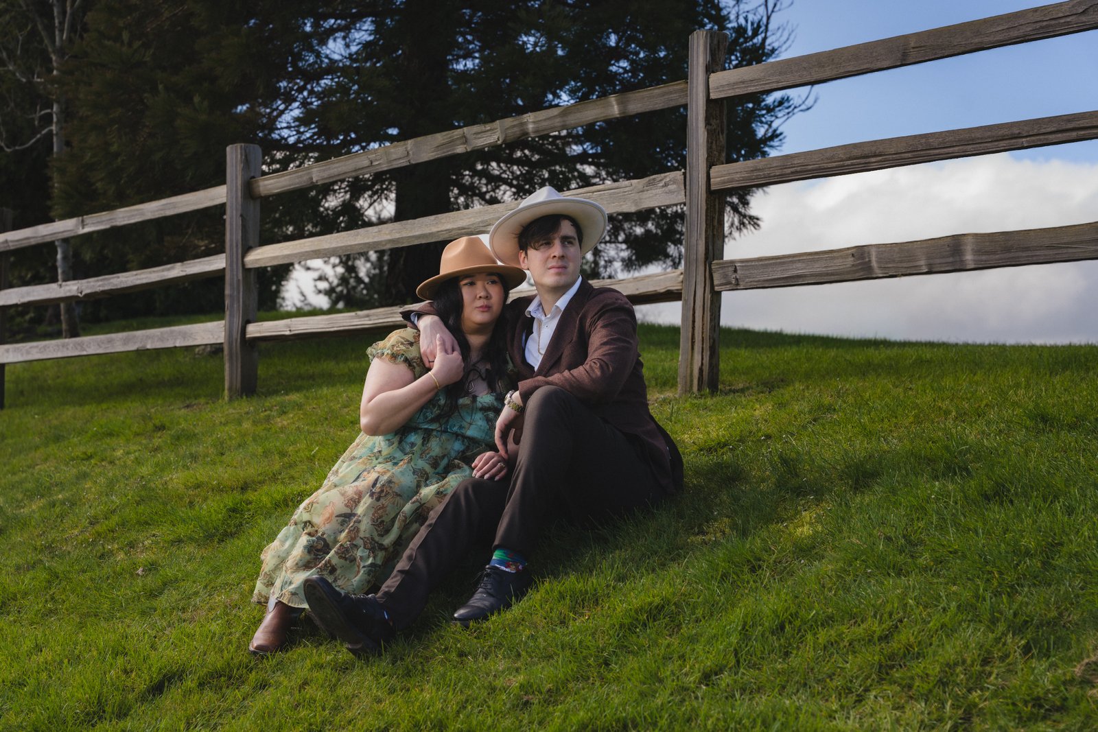 Couple sitting together by a wooden fence on a grassy hill