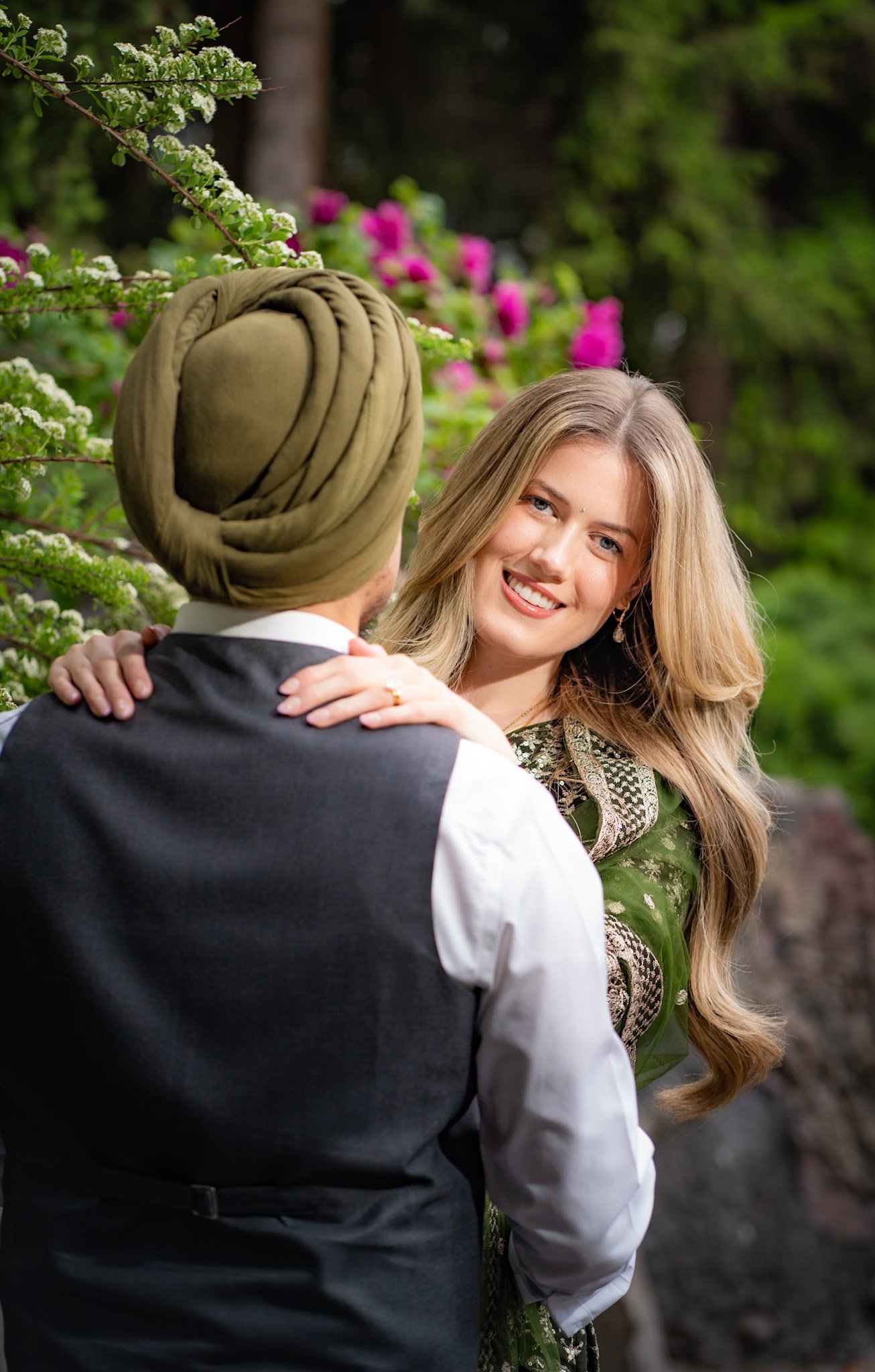 Groom in a green turban embracing his smiling partner in a garden